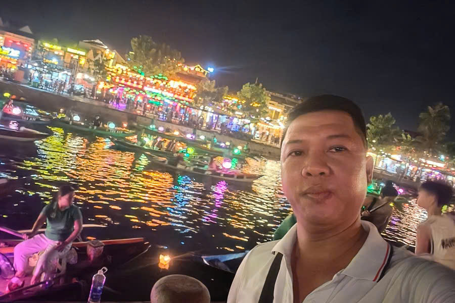 Viet Nguyen taking a selfie with colorful lantern boats on the Thu Bon River in Hoi An.