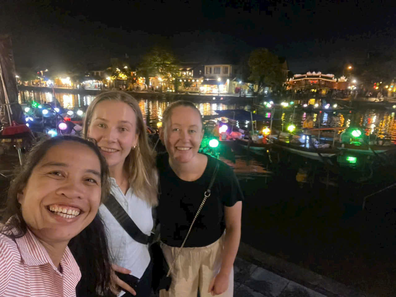 Travelers taking a nighttime selfie by the lantern boats in Hoi An, Vietnam