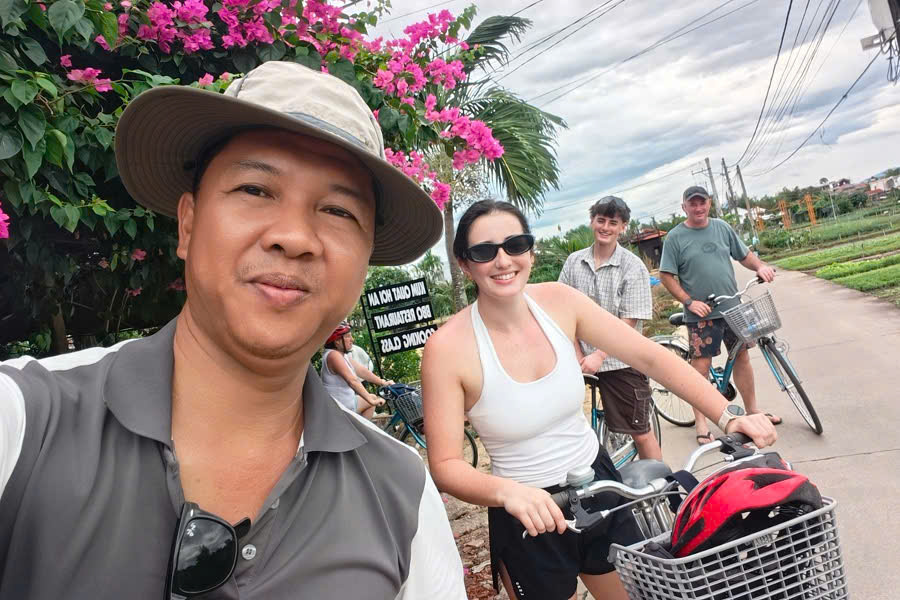 Viet Nguyen poses with guests at Tra Que Organic Vegetable Village during a Hoi An countryside cycling tour through rice fields and local villages.
