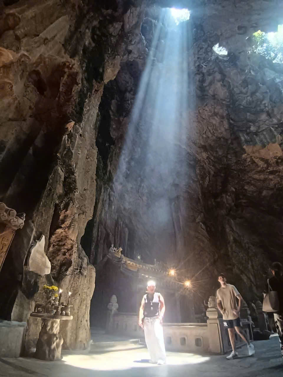 Guest taking photos beneath a beam of sunlight streaming through the roof of Huyen Khong Cave at Marble Mountains, Da Nang.