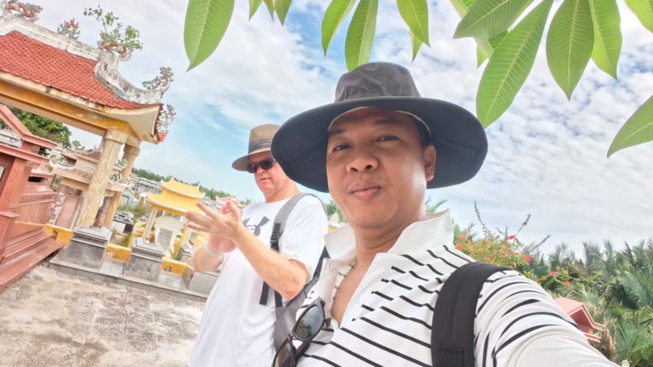 Viet Nguyen taking a selfie with guests during a Hoi An countryside bicycle tour near a traditional village cemetery